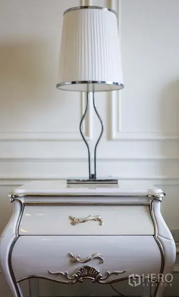 คอนโด ให้เช่าในKhlong Toei, Bangkok - ภาพระยะใกล้ของโต๊ะหัวเตียงสีขาวพร้อมโคมไฟและผนังบัวปั้น