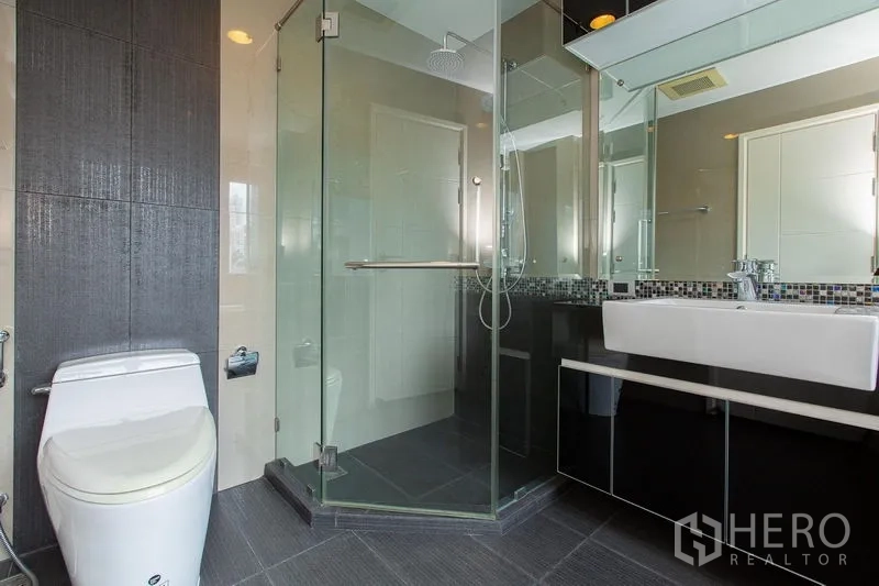 公寓 出租在Khlong Toei, Bangkok - 当代浴室配玻璃淋浴间、马赛克背墙与挂墙式马桶。