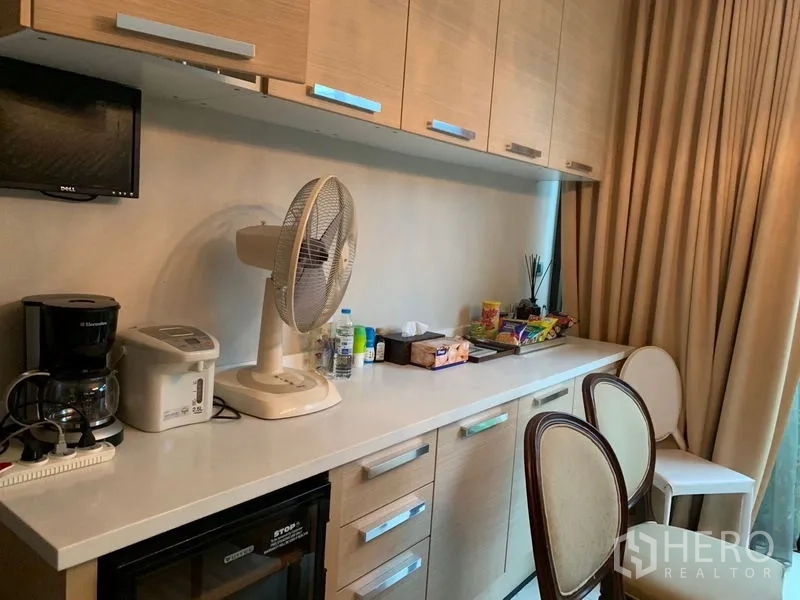 Townhouse for sale in Watthana, Bangkok - Pantry with long countertop, light wood cabinets and small appliances beside full-height curtains.