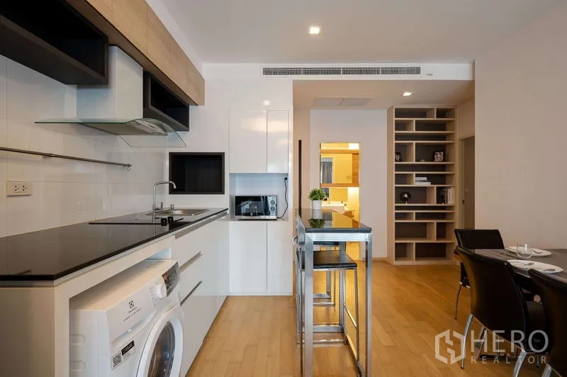 คอนโด ขายในWatthana, Bangkok - ครัวแบบเปิดพร้อมเคาน์เตอร์ท็อปสีดำ ไอส์แลนด์ เตาไฟฟ้า เครื่องซักผ้า และมุมทานอาหารพื้นไม้