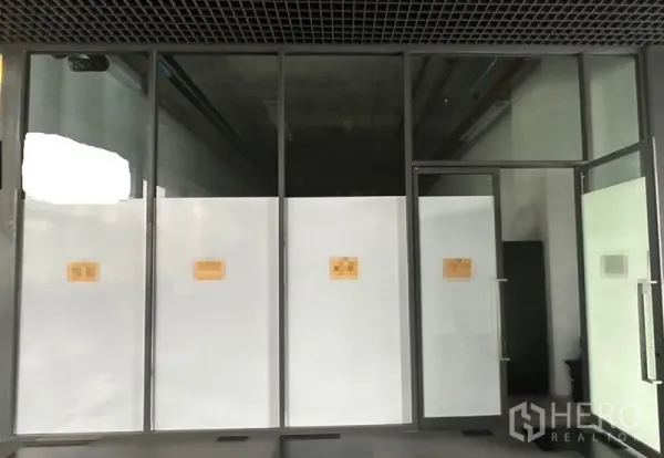 零售空间 出租在Khlong Toei, Bangkok - 空置商铺的整面玻璃门头，带金属框门与磨砂贴膜。