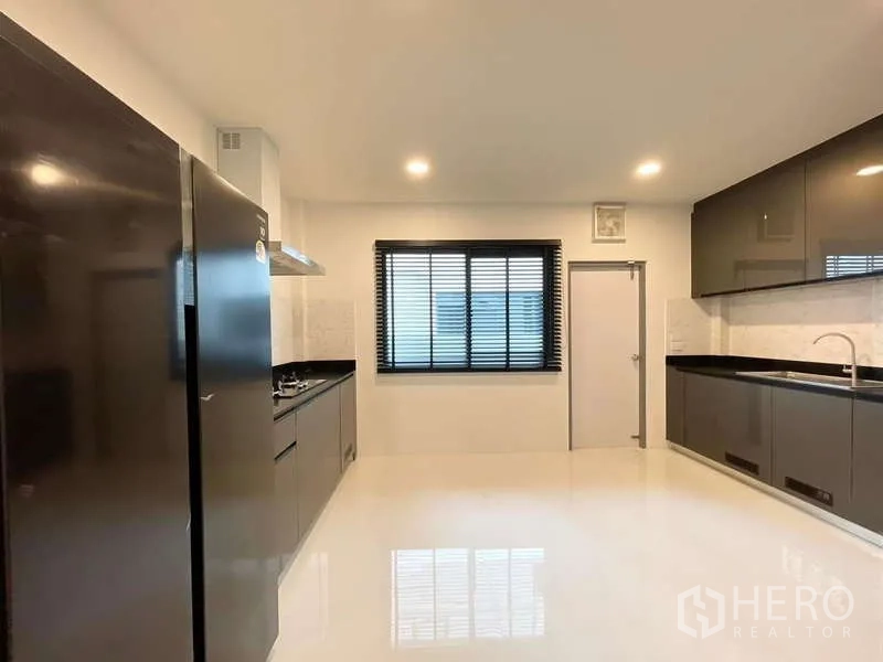 Detached House for rent in Bang Phli, Samut Prakan - Large enclosed kitchen with glossy cabinets, black countertops, range hood and fridge.