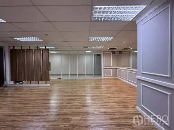 Office Space for rent - Open-plan office area with glass partition wall and wood slat divider under fluorescent lighting.