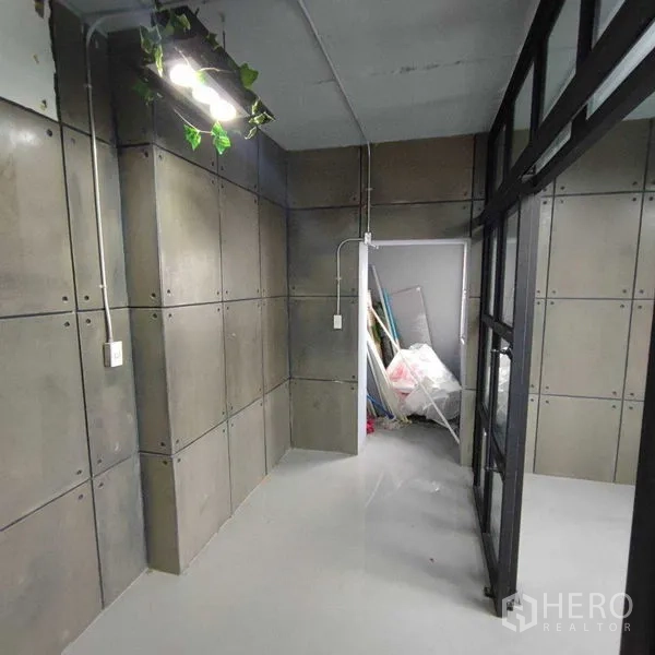 办公空间 出租在Watthana, Bangkok - 狭窄通道通向后室，混凝土板墙与藤蔓吊灯。