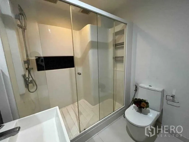 Condominium for sale - Bathroom view showing walk-in shower, toilet, and built-in shelving behind clear glass.