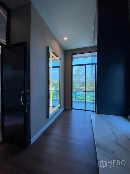 Detached House for sale in Don Mueang, Bangkok - Hallway to the balcony with illuminated mirror and large glass door overlooking greenery.
