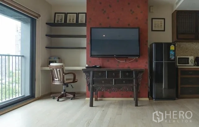 คอนโด ให้เช่าในKhlong Toei, Bangkok - พื้นที่นั่งเล่นมีทีวีติดผนัง โต๊ะทำงาน ชั้นวาง และระเบียงชมวิวเมือง