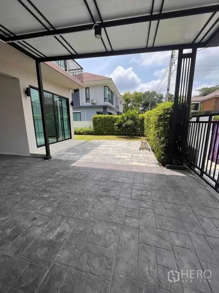 Detached House for rent or sale in Thanyaburi, Pathum Thani - Covered carport and paved driveway behind a black metal gate.