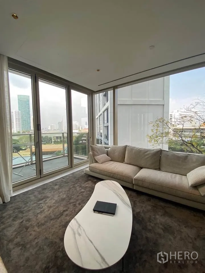 Condominium for rent in Sathon, Bangkok - Corner living room with a plush sofa, marble coffee table, and sliding glass doors.