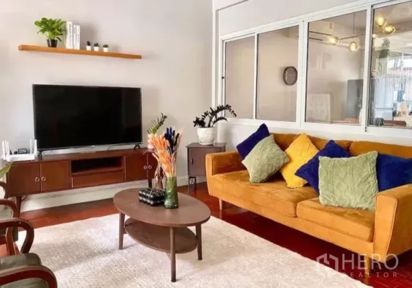 Townhouse for rent in Watthana, Bangkok - Bright lounge with mustard sofa, coffee table, TV unit and wood floors.