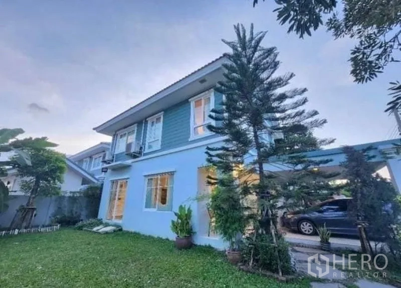 Detached House for rent in Bang Bo, Samut Prakan - Two-storey detached house with lawn garden and covered carport at dusk.