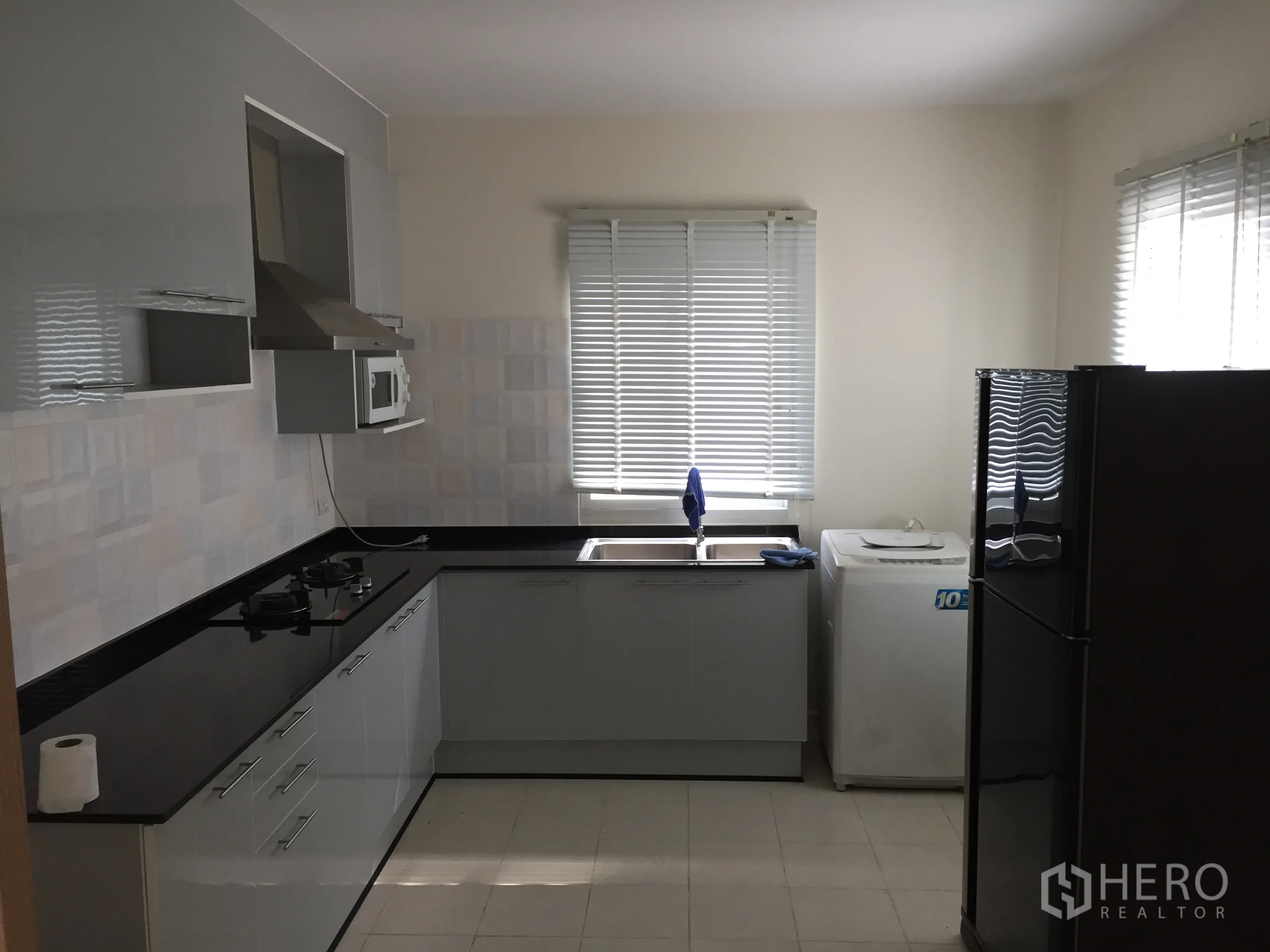 Detached House for rent in Pathum Thani - L-shaped kitchen with black countertops, gas hob, extractor hood, fridge and washing machine.