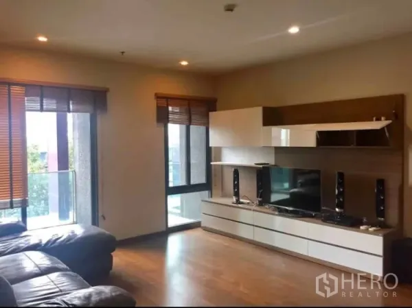 คอนโด ให้เช่าในKhlong Toei, Bangkok - ห้องนั่งเล่นสว่างพื้นไม้ ตู้ทีวีบิวท์อิน โซฟาหนัง และหน้าต่างเปิดสู่ระเบียง