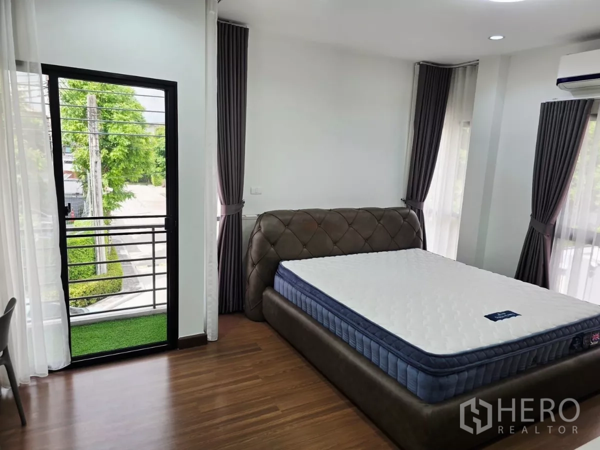 Detached House for rent in Prawet, Bangkok - Master bedroom with upholstered bed, balcony access and wood floors.