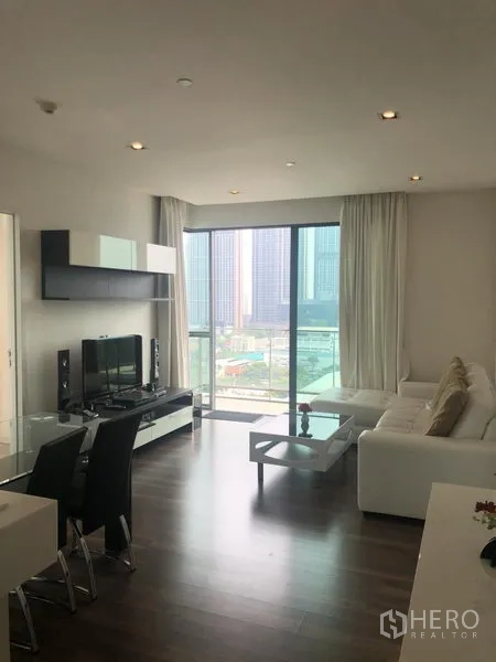 Condominium for rent or sale in Phra Khanong, Bangkok - Open-plan lounge and dining room leading to a glass balcony with city view in a modern Phra Khanong condominium.