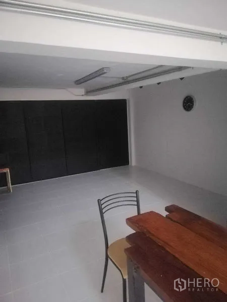Shophouse for rent in Khlong Toei, Bangkok - Open-plan ground level with white tile floor, black folding doors and a wooden table.