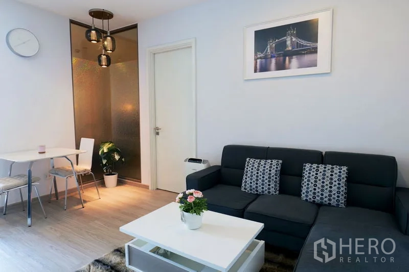 คอนโด ให้เช่าในWatthana, Bangkok - ห้องนั่งเล่นสว่าง โซฟาสีเข้ม โต๊ะกลางสีขาว ชุดโต๊ะอาหารเล็ก และโคมไฟเพดาน