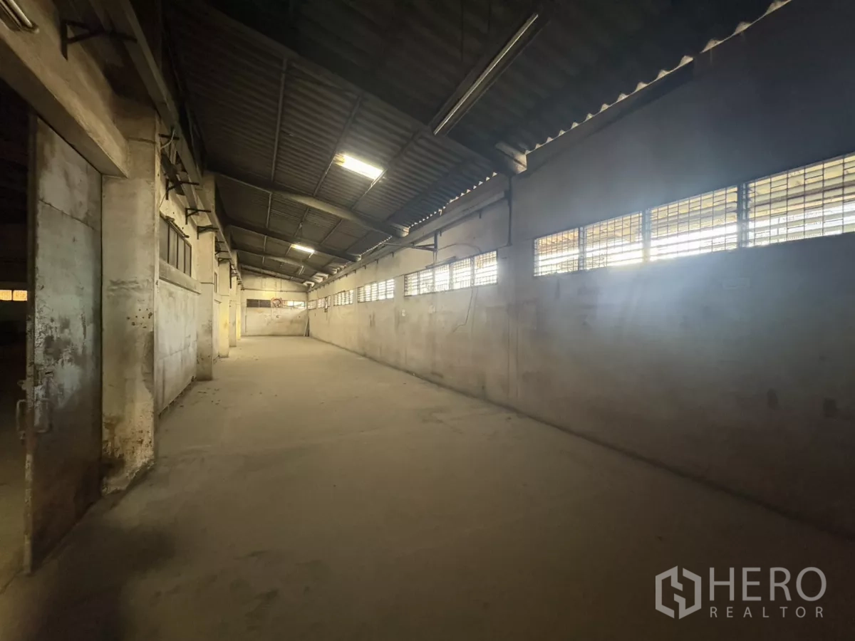 Warehouse for rent in Khlong Toei, Bangkok - Open storage bay featuring a high metal-sheet roof, barred windows and smooth concrete flooring.