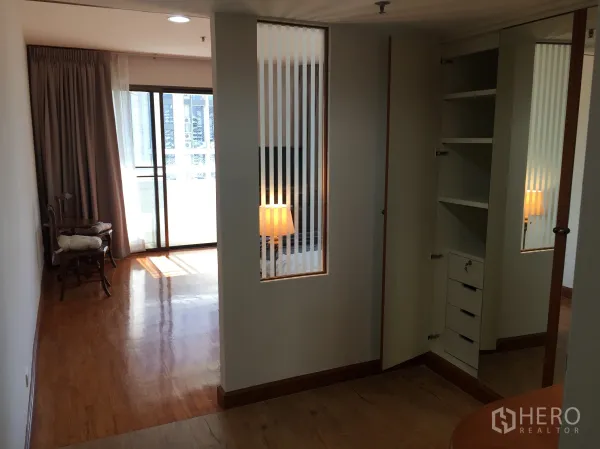 Condominium for sale in Watthana, Bangkok - Hallway leading to a balcony through a sliding glass door, with mirrored wardrobe, built-in storage and polished wood floors.