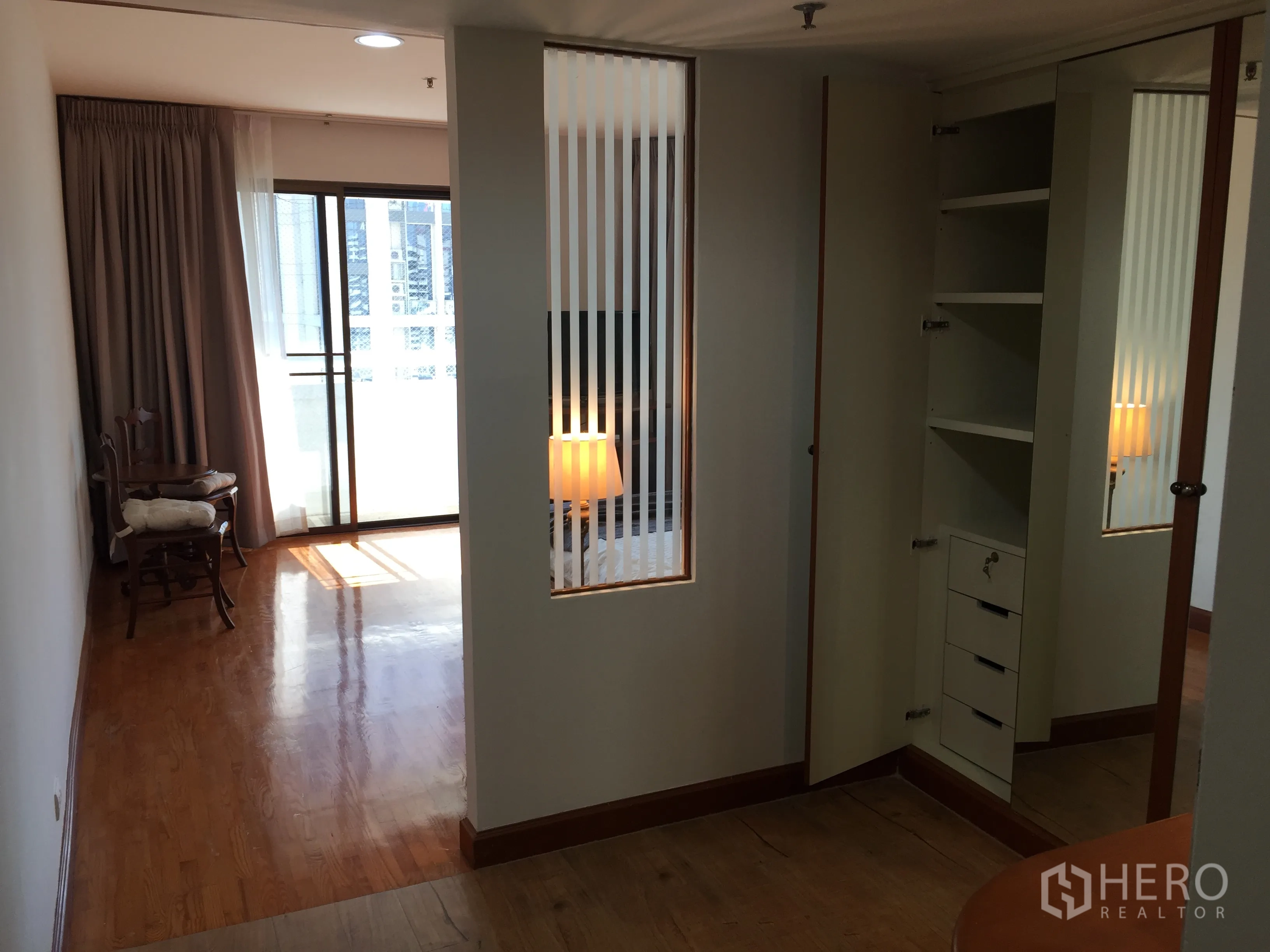 Condominium for sale in Watthana, Bangkok - Hallway leading to a balcony through a sliding glass door, with mirrored wardrobe, built-in storage and polished wood floors.