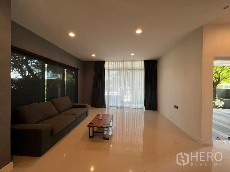 บ้าน ให้เช่าหรือขายในBang Kapi, Bangkok - ห้องนั่งเล่นมีโซฟา โต๊ะกลาง และประตูกระจกสูงจากพื้นถึงเพดานเปิดสู่สวน