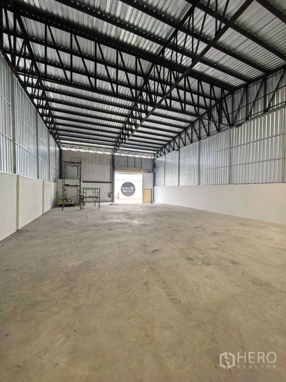 Warehouse for rent in Suan Luang, Bangkok - Reverse view toward the entrance showing open floor area, steel roof trusses, and scaffolding.