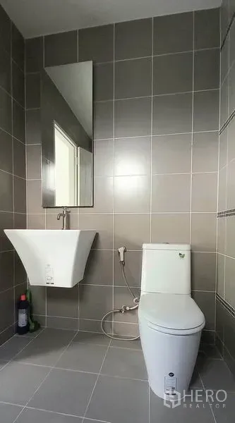 ทาวน์เฮาส์ ขายในMueang Pathum Thani, Pathum Thani - ห้องน้ำสไตล์โมเดิร์น ปูกระเบื้องสีเทา อ่างล้างหน้าแขวนผนัง กระจก และโถสุขภัณฑ์พร้อมสายฉีด