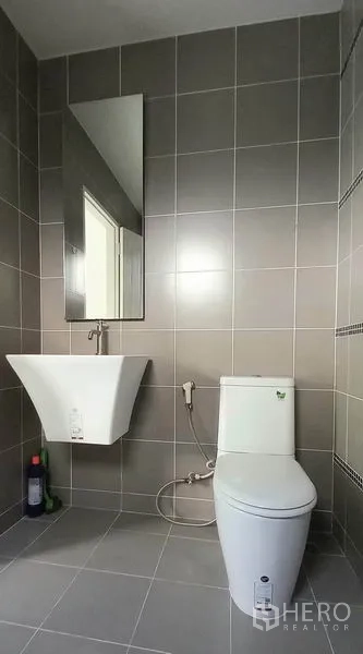 ทาวน์เฮาส์ ขายในMueang Pathum Thani, Pathum Thani - ห้องน้ำสไตล์โมเดิร์น ปูกระเบื้องสีเทา อ่างล้างหน้าแขวนผนัง กระจก และโถสุขภัณฑ์พร้อมสายฉีด