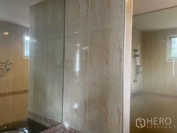 บ้าน ให้เช่าในHuai Khwang, Bangkok - ห้องน้ำกรุกระเบื้องสีเบจ ฉากกั้นกระจก เคาน์เตอร์อ่างล้างหน้า และหน้าต่างระบายอากาศ.