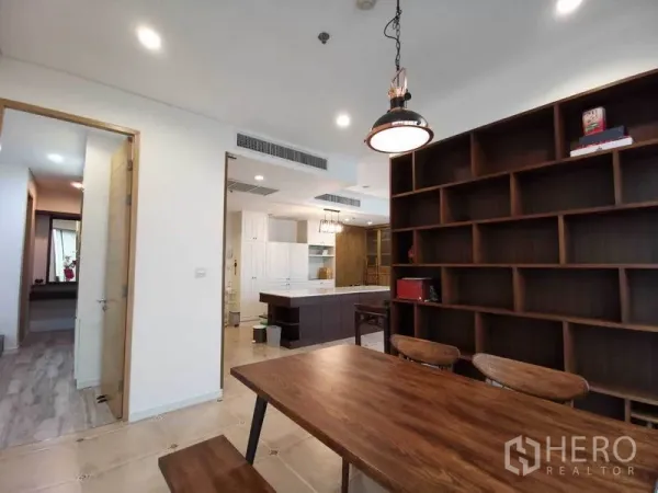 Condominium for rent or sale in Bang Rak, Bangkok - Open-plan dining area with pendant light, large wooden bookshelf, and view to a modern kitchen island.