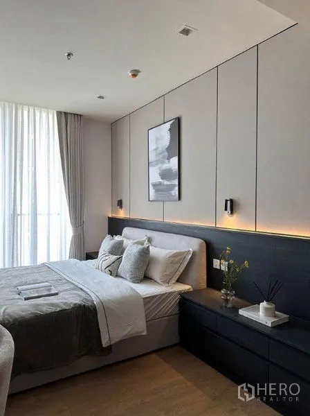 Condominium for rent in Watthana, Bangkok - Bedroom from another angle showing panelled headboard wall, warm LED strip lighting and sheer curtains.