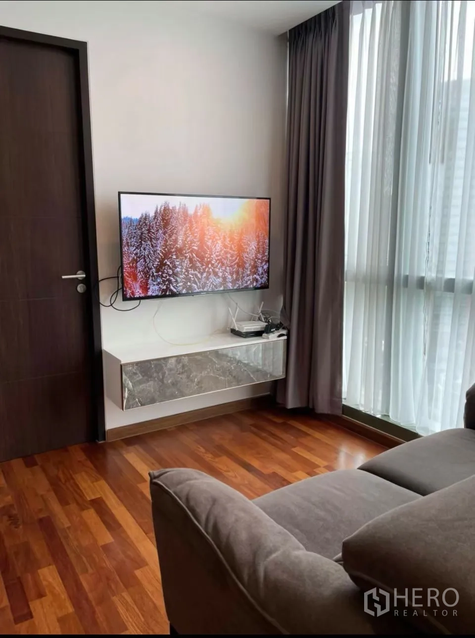 คอนโด for rent in Ratchathewi, Bangkok - ทีวีแขวนผนังและชั้นลอยตรงข้ามโซฟาใกล้หน้าต่างสูงพร้อมผ้าม่าน