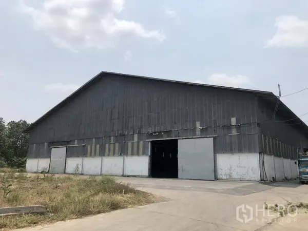 Warehouse for rent in Nonthaburi - Large corrugated metal warehouse exterior with wide sliding doors and driveway.