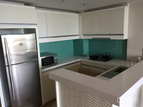 Condominium for rent or sale in Sathon, Bangkok - Modern U-shaped kitchen with turquoise glass backsplash, stainless refrigerator, microwave and cooktop.