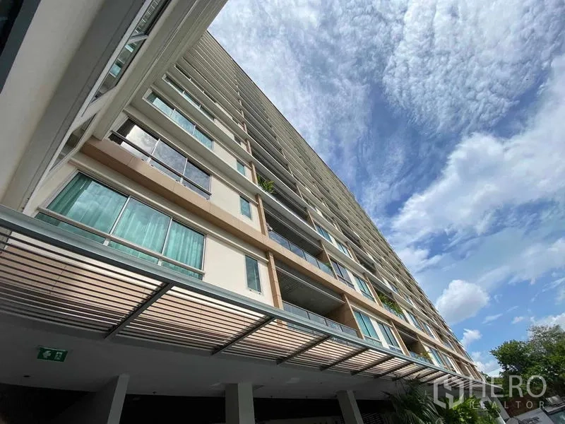 Condominium for rent in Yan Nawa, Bangkok - Upward view of the high-rise condominium facade under a bright blue sky.