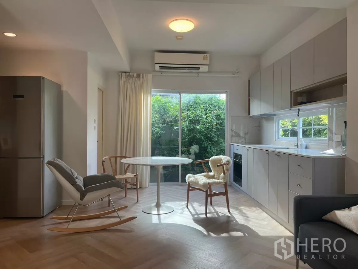Townhouse for rent in Bang Phli, Samut Prakan - Light grey kitchen with sliding glass door to greenery and round dining table.