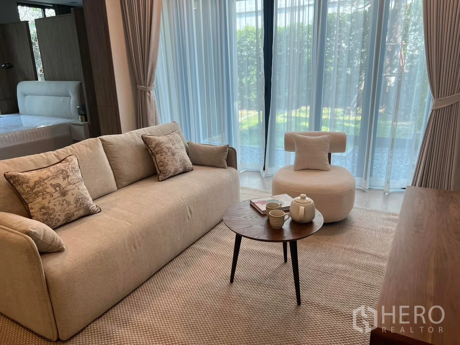 独栋房屋 for rent or sale in Saphan Sung, Bangkok - 温馨客厅配米色沙发、圆椅与茶几，大幅落地窗面向花园。