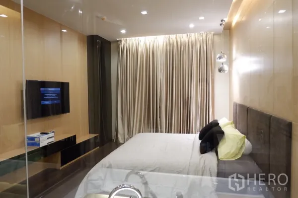 公寓 出租在Watthana, Bangkok - 卧室视角，可见壁挂电视、长窗帘与内置电视柜，灯光柔和。