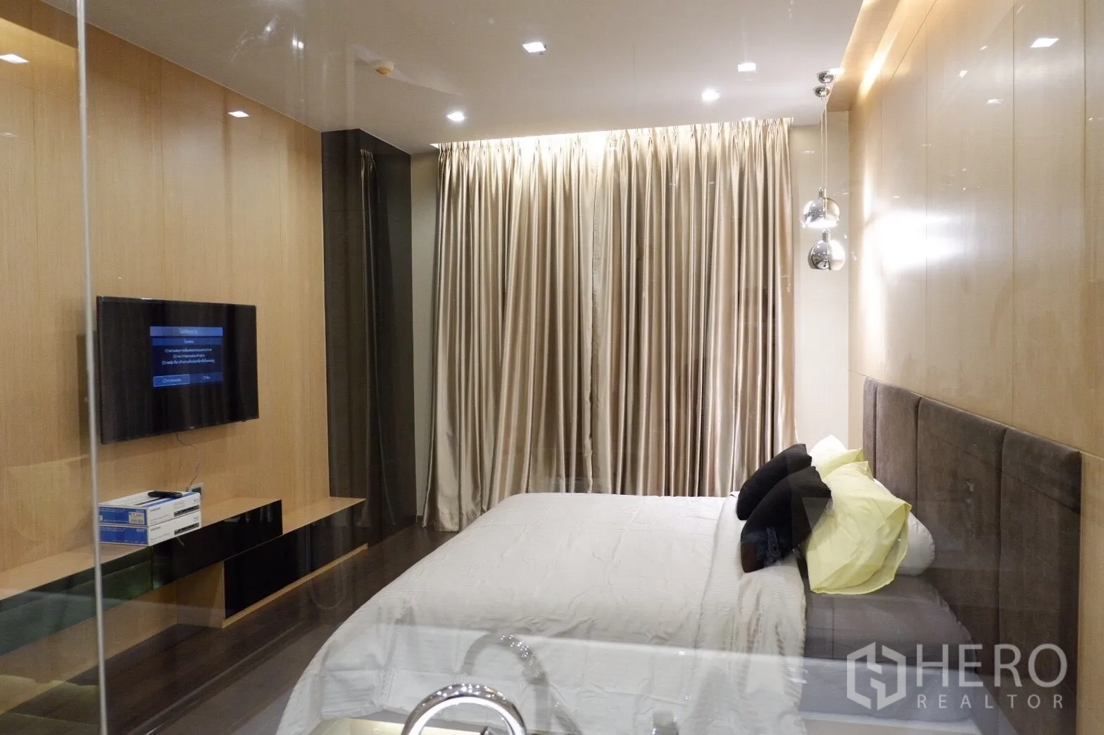 公寓 出租在Watthana, Bangkok - 卧室视角，可见壁挂电视、长窗帘与内置电视柜，灯光柔和。