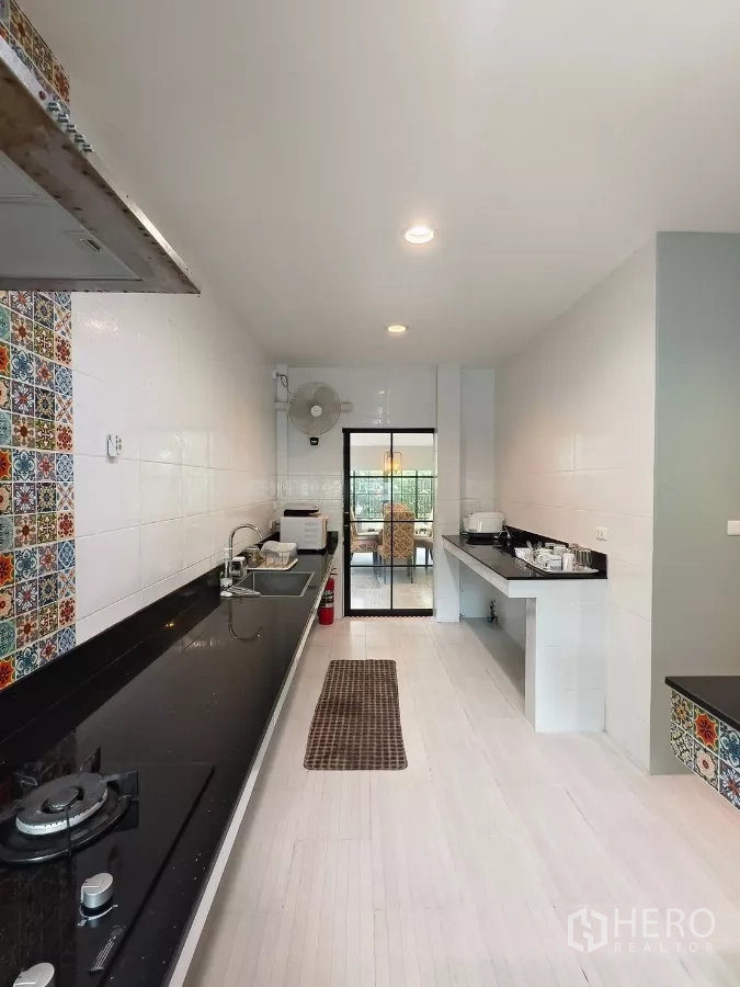 Detached House for rent in Bang Kapi, Bangkok - Galley kitchen with long black countertops and sliding door to dining.