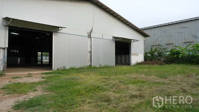 Factory for rent in Bang Phli, Samut Prakan - Side exterior of metal-clad warehouse with large sliding doors and open yard.