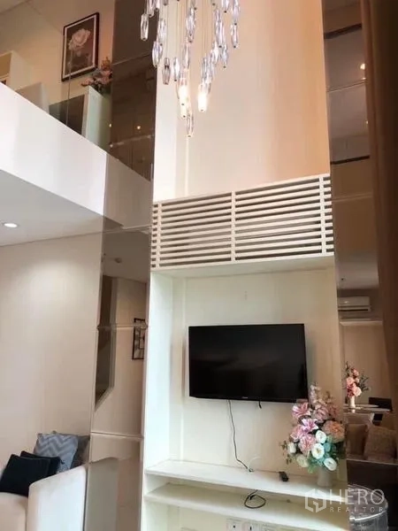 公寓 出租在Ratchathewi, Bangkok - 挑高客厅展示水晶吊灯与电视墙，楼上为夹层。
