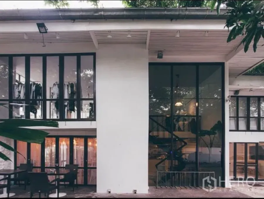 零售空间 出租在Khlong Toei, Bangkok - 现代两层零售建筑，落地玻璃、可见螺旋楼梯与树荫下的室外座位。