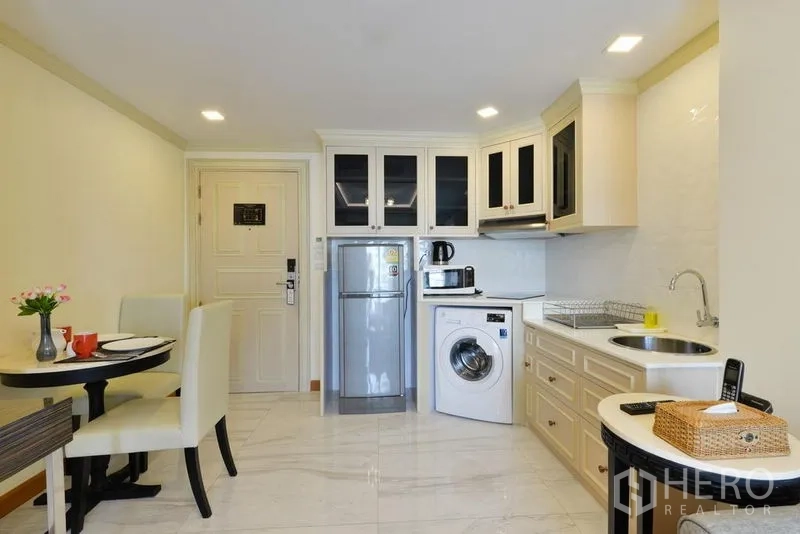 房间 出租在Khlong Toei, Bangkok - 紧凑厨房，白色橱柜、冰箱、洗衣机、微波炉与小餐桌。