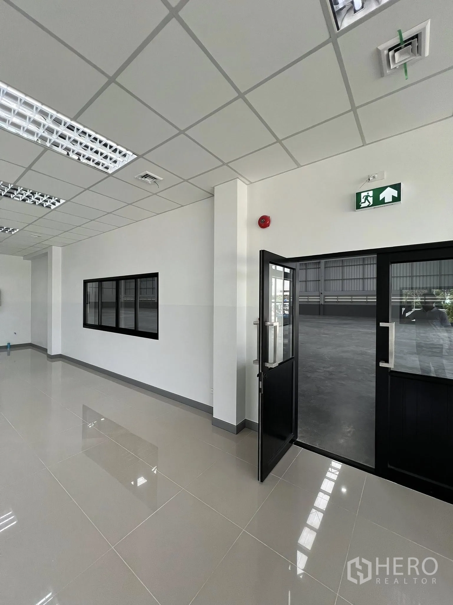 Warehouse for rent in Phra Pradaeng, Samut Prakan - Office entrance with emergency exit sign opening to the warehouse floor.