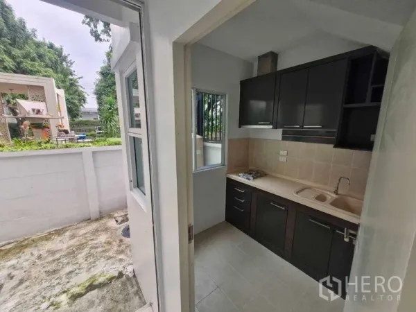 独立式住宅 出售在Rat Burana, Bangkok - 配有深色橱柜的厨房，带灶台与通往后院的门