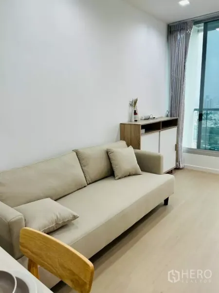 公寓 出租在Bang Rak, Bangkok - 米色沙发靠大窗，远眺城市景观，旁有边柜与浅木地板。