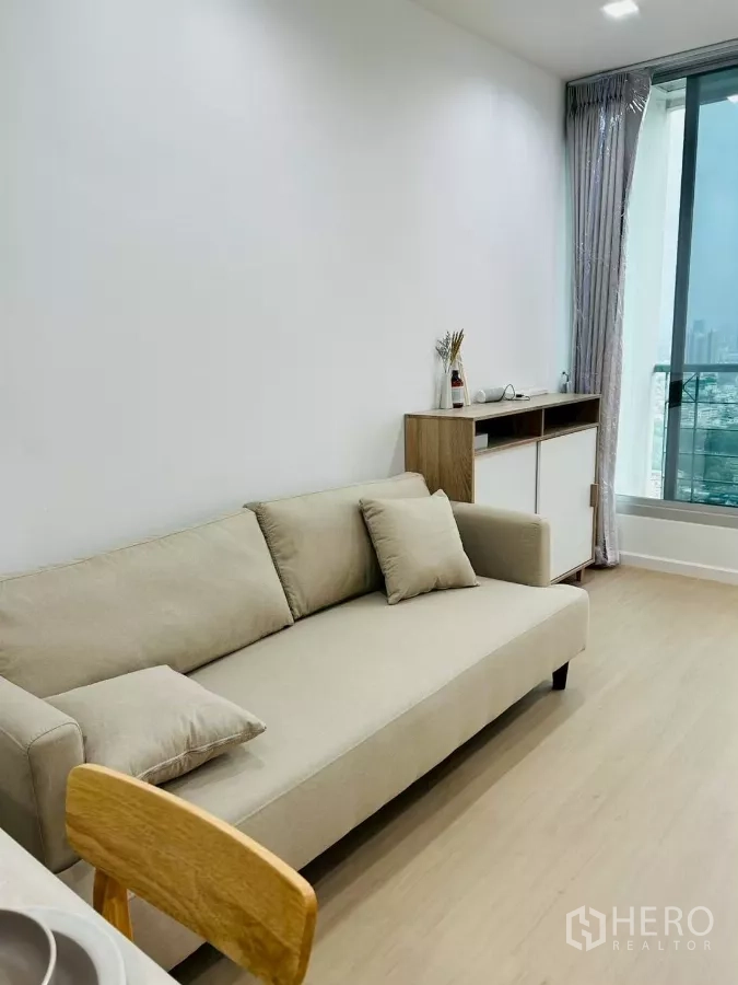 公寓 出租在Bang Rak, Bangkok - 米色沙发靠大窗，远眺城市景观，旁有边柜与浅木地板。