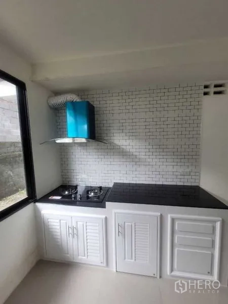 Detached House for rent in Prawet, Bangkok - Separate Thai kitchen with gas hob, chimney hood and white cabinets with subway tile backsplash.