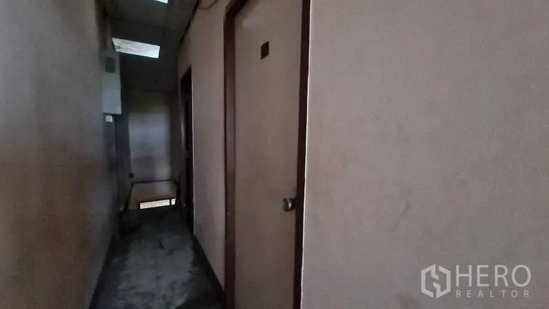 Shophouse for sale in Watthana, Bangkok - Dim corridor with doors to multiple rooms and stair access.